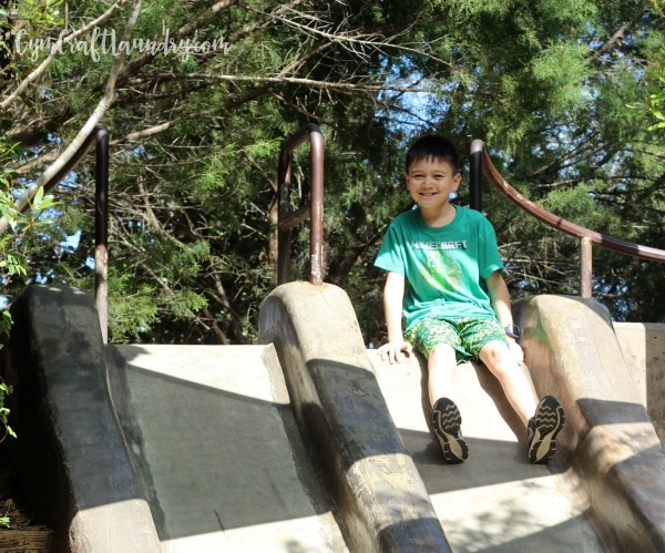 Boy, sweaty from outdoor playtime, is at the top of a slide.